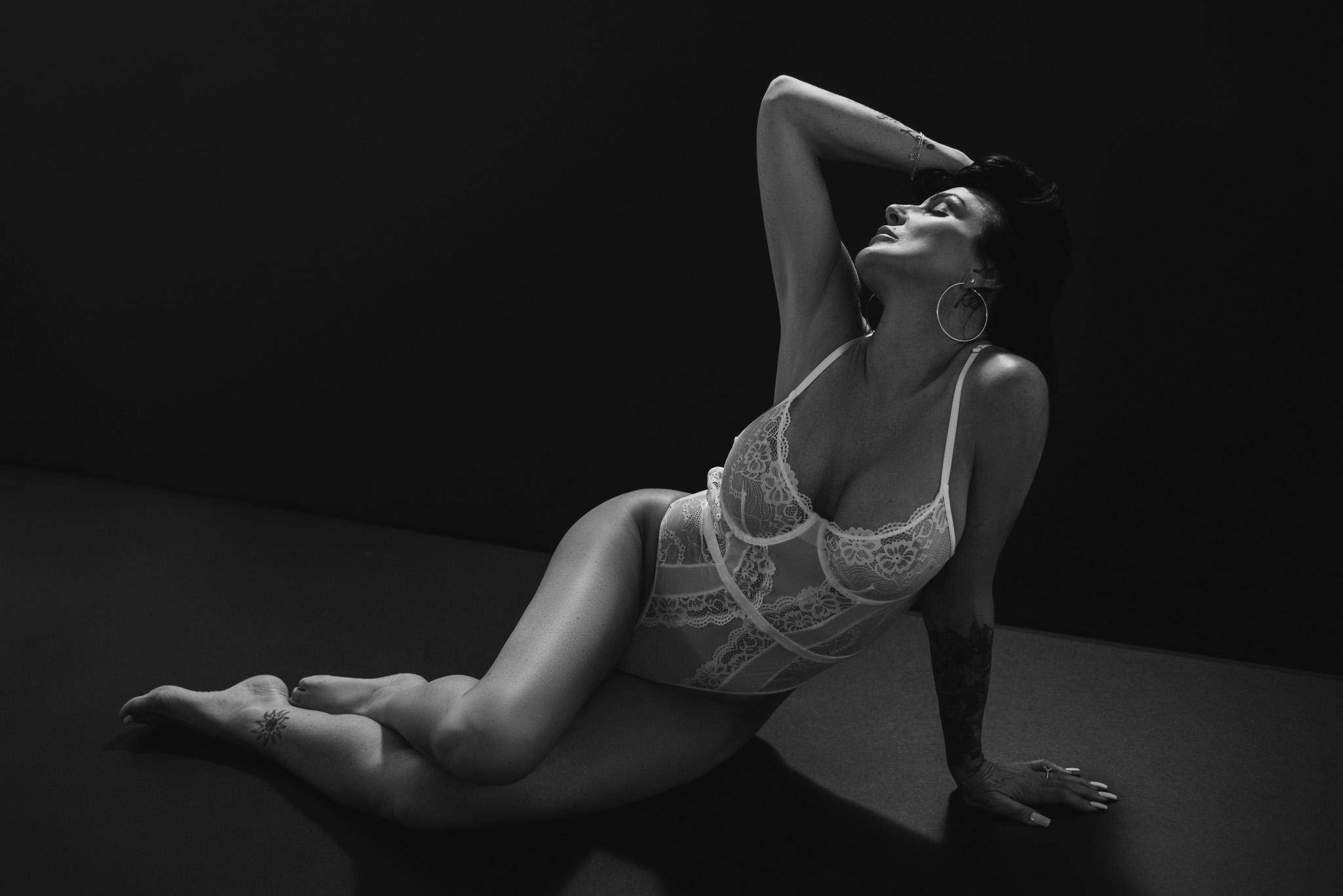 Black and white image of a woman sitting on black background wearing white lingerie