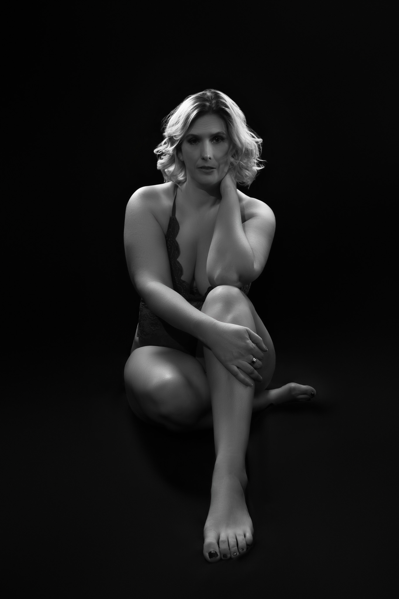 Elegant black and white boudoir portrait featuring woman seated in dramatic studio light.