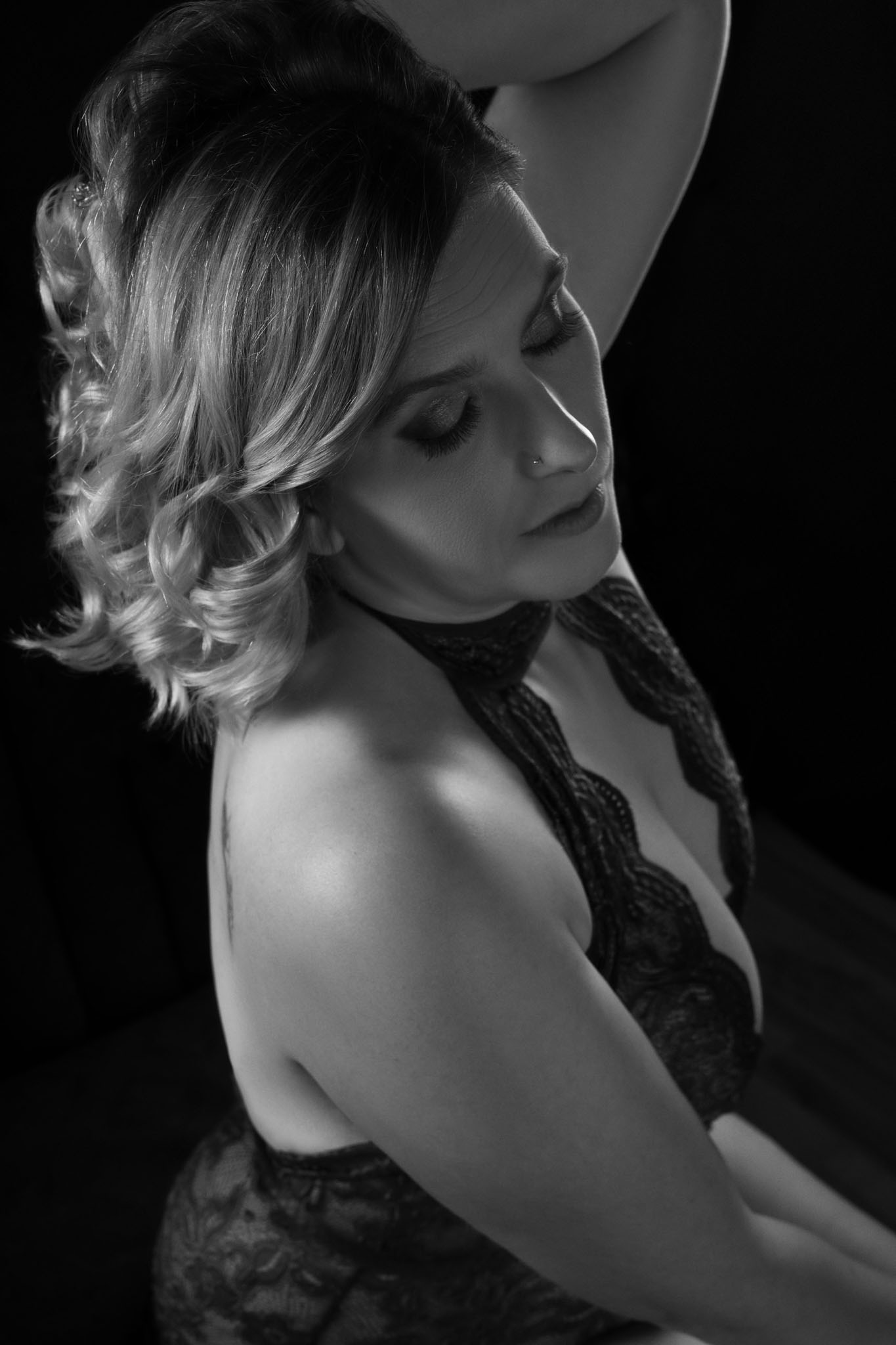 Black and white boudoir portrait of woman seated against dark background, softly lit.